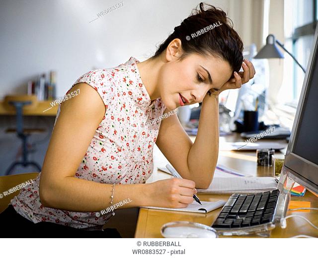 Profile of a young woman writing on a notepad in an office