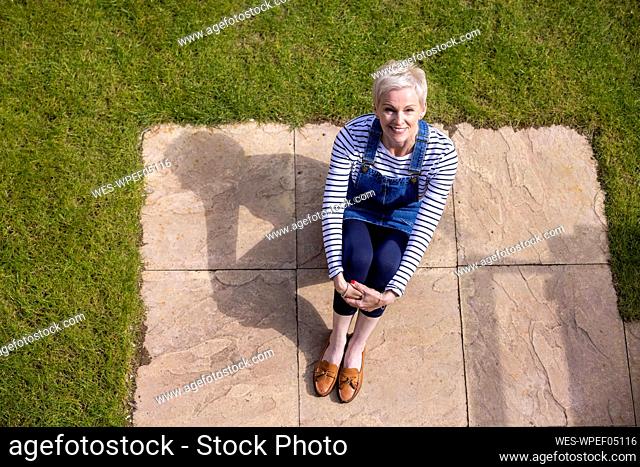 Smiling woman hugging knees while sitting at garden