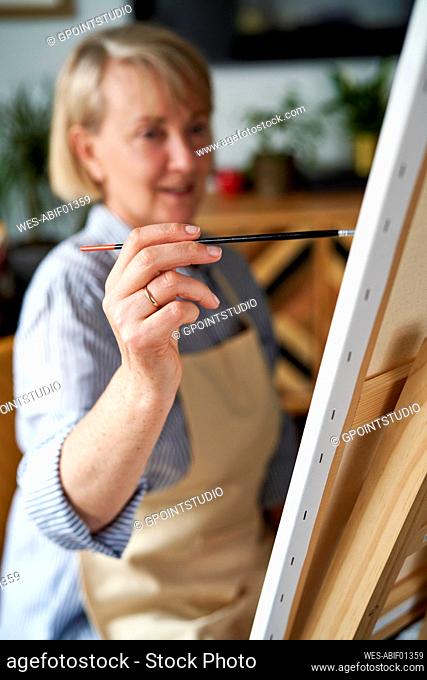 Mature woman making painting on easel at home