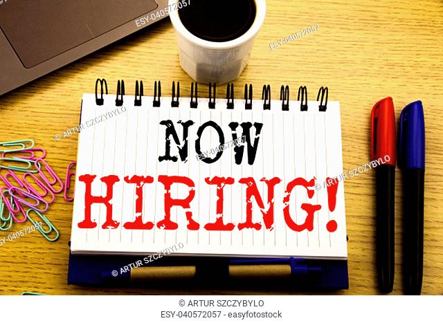 Hand writing text caption showing Now Hiring. Business concept for Hire Recruitment written on notebook on the wooden background in the Office with laptop...