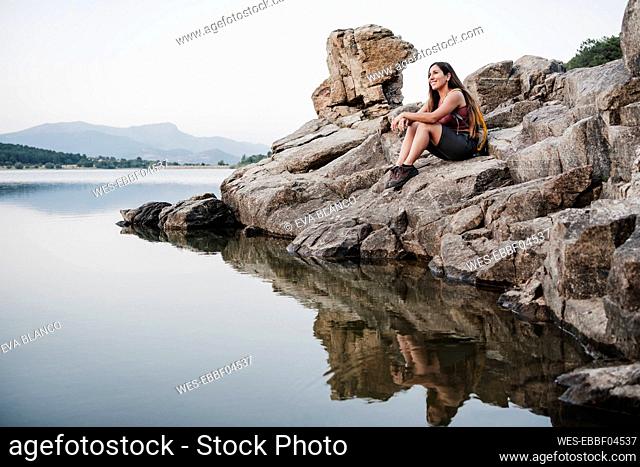 Smiling female hiker looking away while sitting on rock at lake
