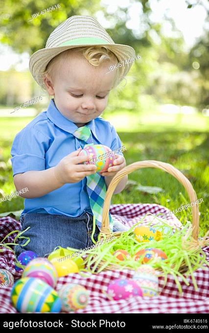 Cute little boy wearing hat enjoying his easter eggs on picnic blanket outside in the park