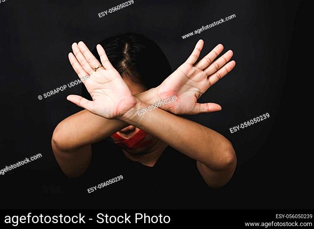 Woman blindfold wrapping mouth with red adhesive tape and show hand sign stop abusing violence and abuse on black background, Human trafficking and abuse