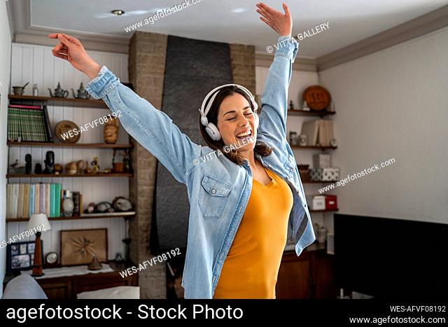 Cheerful woman with headphones enjoying music while standing in living room