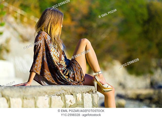 Young woman sitting on wall atop beach watching sunset