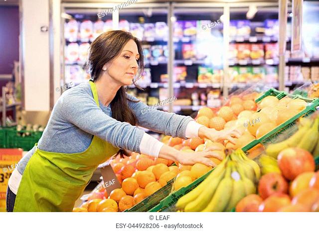 Beautiful mature saleswoman arranging oranges in supermarket