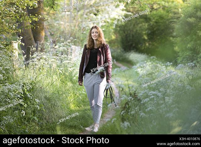Jeune femme se promenant avec son chien sur un petit sentier de campagne borde d'ombelliferes en lisiere de foret, Departement d'Eure-et-Loir