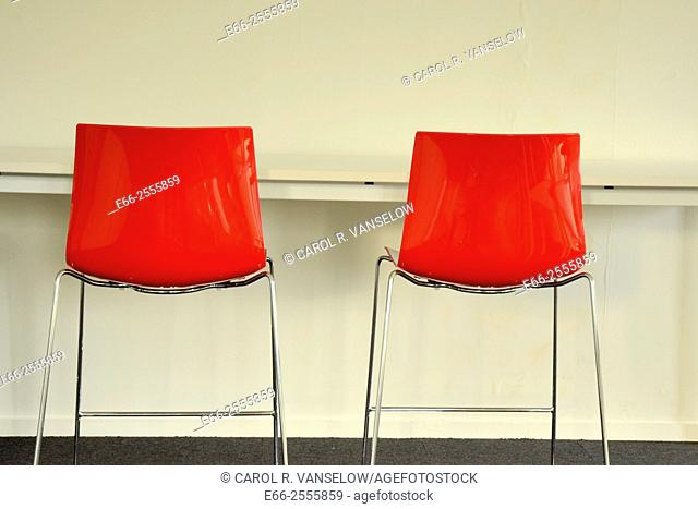 two red chairs by table against a white wall