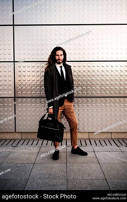 Entrepreneur wearing suit carrying briefcase while standing against silver wall