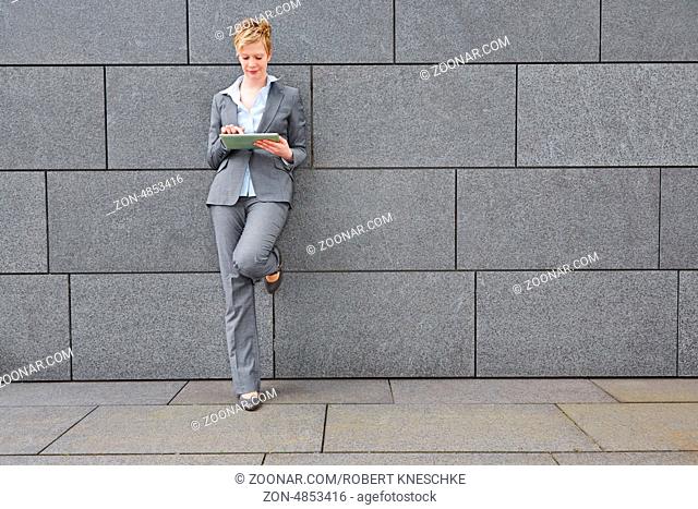 Frau in der Stadt mit einem Tablet PC lehnt an einer Mauer