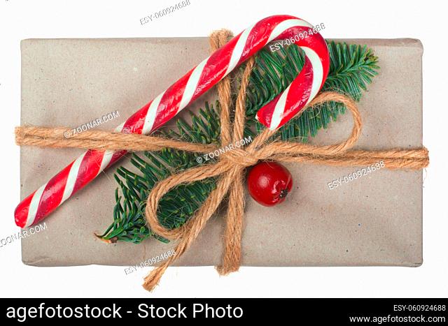 Wrapped vintage christmas gift box in craft paper with rope bow, striped candy cane fir tree twig and red berry isolated on white
