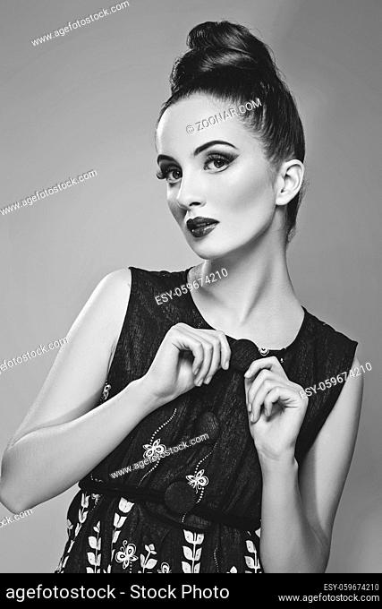 Beautiful young woman with hairdo and bright make-up. Doll style. Beauty shot on grey background. Copy space. Monochrome