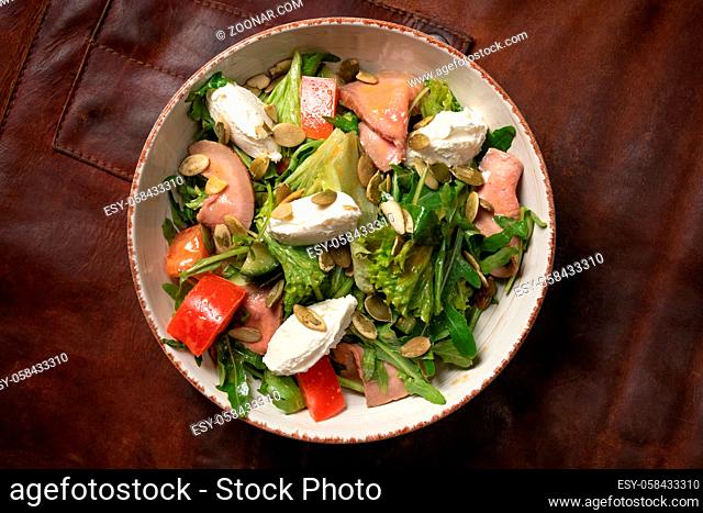 Salmon fresh vegetable salad with mozzarella cheese stands on a table covered with a leather rag and a decorative detail of a simple mechanism
