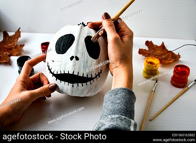 Woman paints face on orange pumpkin for Halloween. Autumn leaves. Diy children craft. Do it yourself. Autumn party decorations