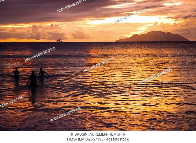 Seychelles, Mahe Island, Beau Vallon, swimming at sunset, Silhouette Island and a sailboat in background, Beau Vallon beach