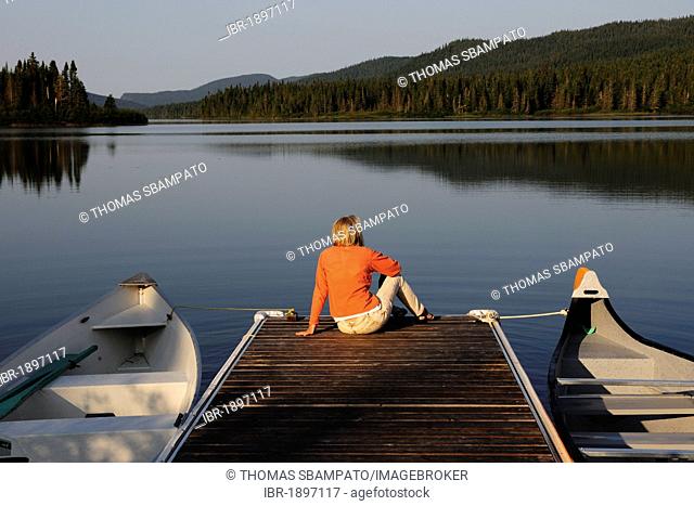 Woman sitting on a jetty overlooking a lake, Gaspésie National Park in the middle of the Chic-Choc Mountains, also known as Shick Shocks, Gaspe Peninsula