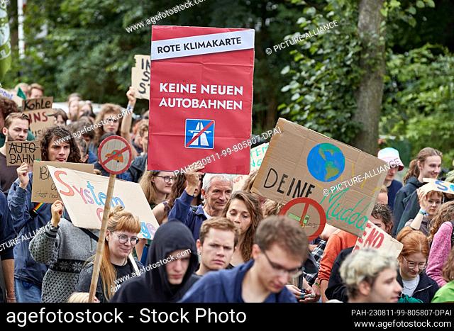 11 August 2023, Lower Saxony, Lüneburg: A participant of a protest march of the climate movement Fridays for Future carries a sign with the inscription ""Red...