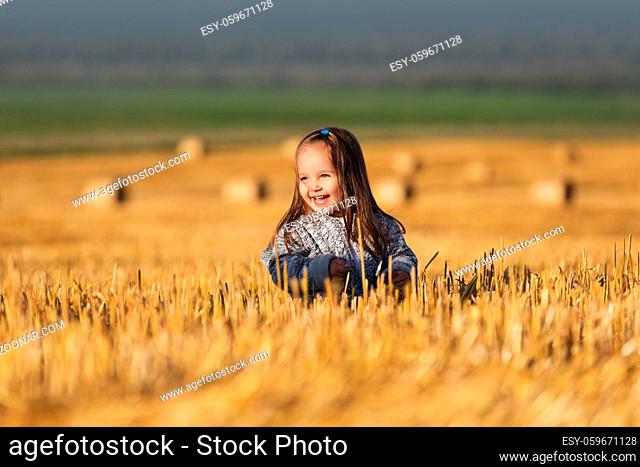 Happy two year old girl walking in a summer harvested field