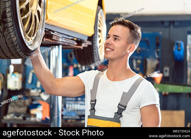 Portrait of a car tuning specialist smiling, while checking the wheels of a tuned lifted car with cool modified rims in a trendy automobile repair shop