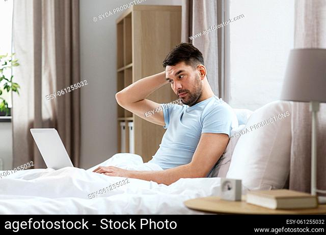 man with laptop in bed at home bedroom