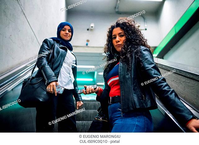 Young woman in hijab with friend moving up subway escalator