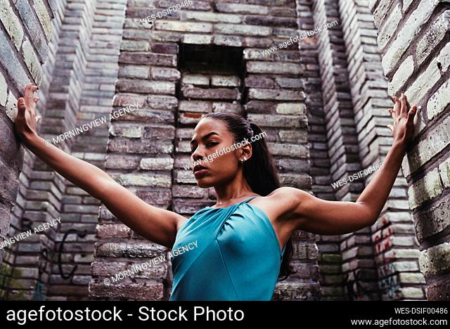 Confident female dancer with arms outstretched amidst stone walls