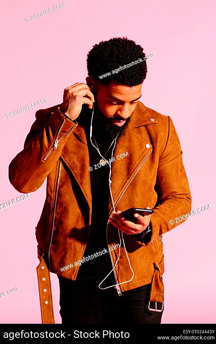 Handsome and cool African American man with beard, listening music, texting, isolated on pink studio background