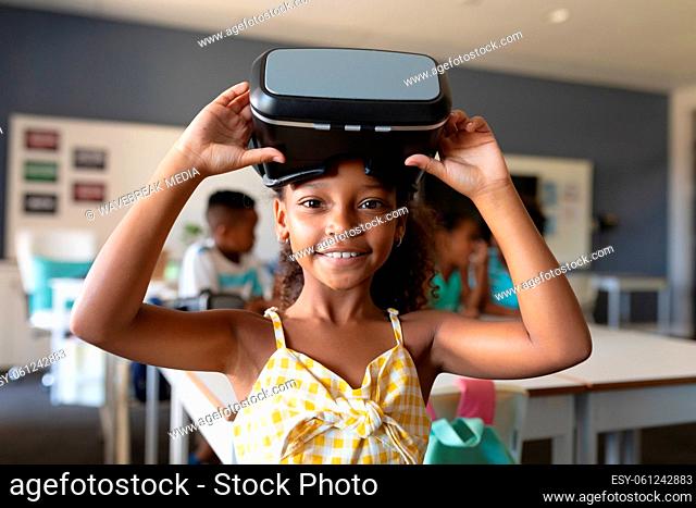Portrait of smiling african american elementary schoolgirl with vr glasses in classroom