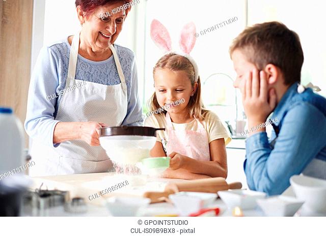 Girl and grandmother sifting flour for easter bake at kitchen counter