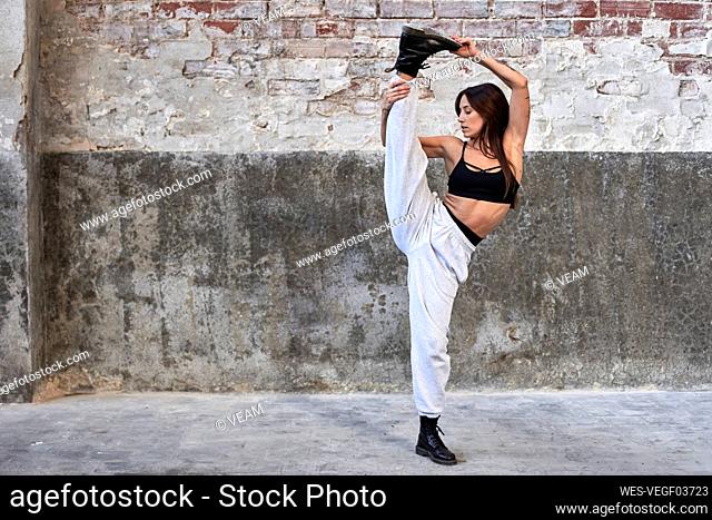 Female dancer standing on one leg against weathered wall in factory