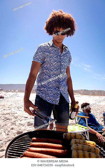 Young man cooking Corn and sausage on barbecue at beach in the sunshine