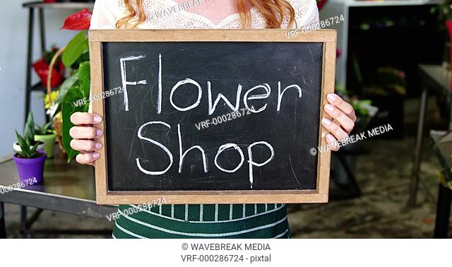 Smiling florist holding flower shop sign on slate