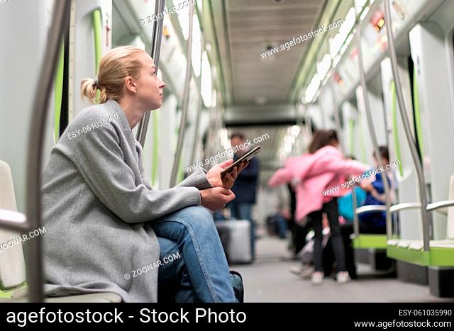 Beautiful blonde caucasian woman wearing winter coat and jeans using smart phone while traveling by metro. Public transportation concept