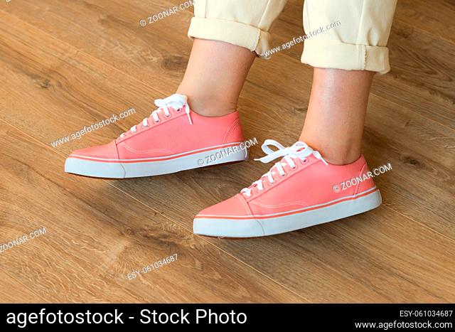 Casual pink shoes sneakers on women?s feet on wooden floor background