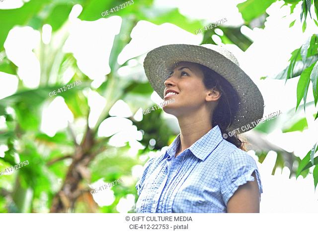 Smiling woman wearing straw hat looking at plants in sunny garden
