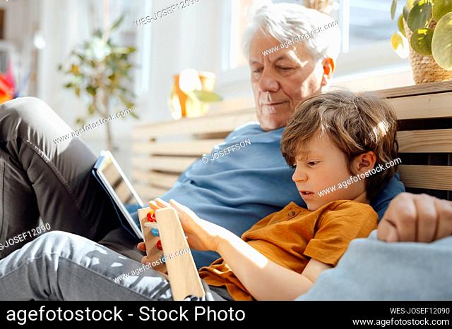 Grandfather looking at grandson with abacus sitting on sofa