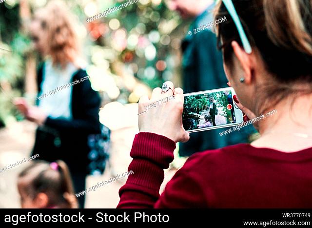 Young woman holding smartphone, looking at phone screen, recording a family trip