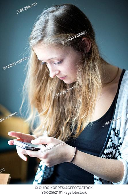 Tilburg, Netherlands. Young, attractive woman reading messages on her smartphone