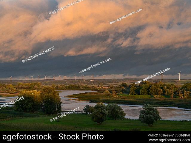 15 October 2021, Brandenburg, Lebus: Dark rain clouds are bathed in a warm light over the German-Polish border river Oder by the light of the evening sun