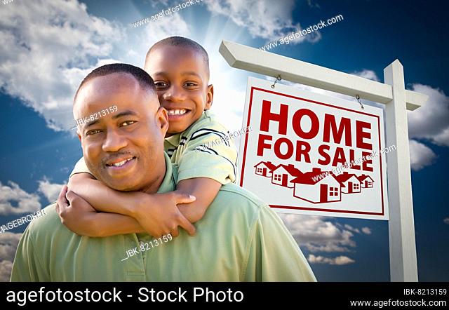 Happy african american father with son in front of home for sale real estate sign and sky