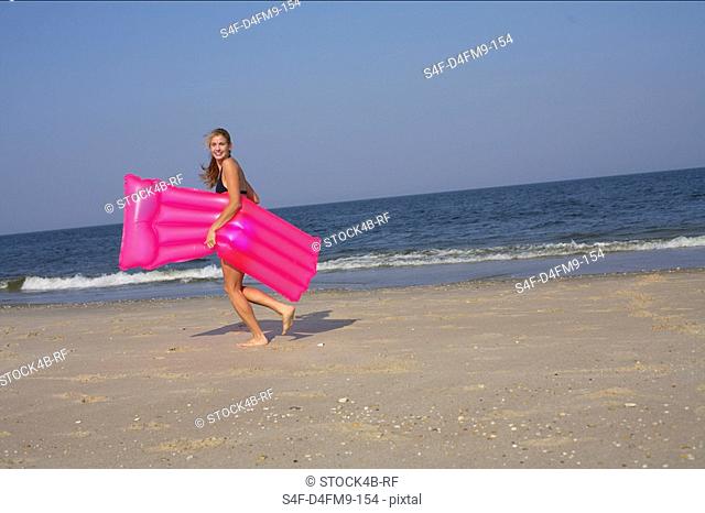 Young woman carrying an airbed at the beach