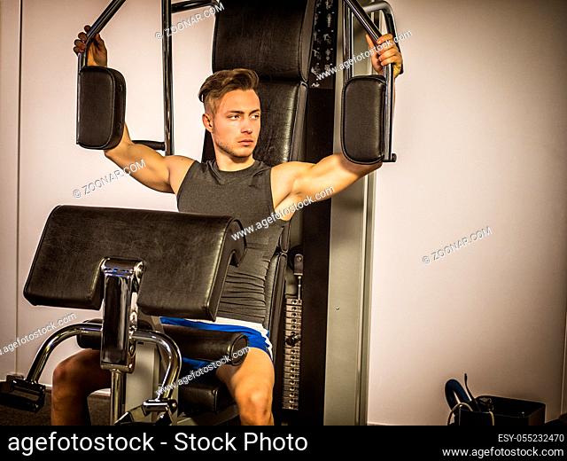 Muscular young man, training pecs on gym cable machine