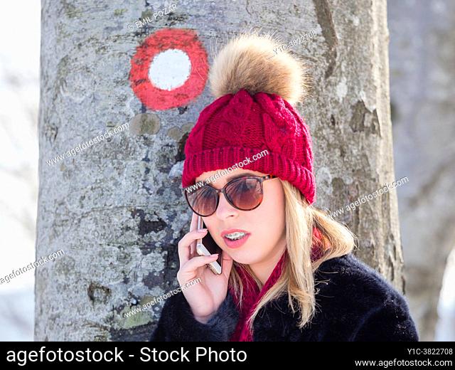 Young woman is inclined on a tree in forest in Winter talking on smartphone
