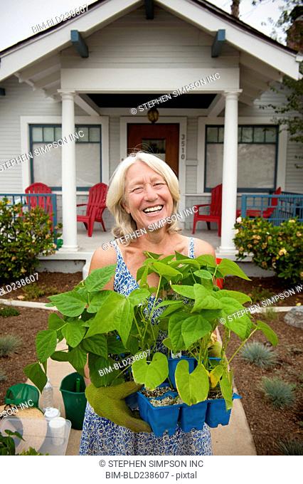 Portrait of smiling Caucasian woman holding tray of plants near house