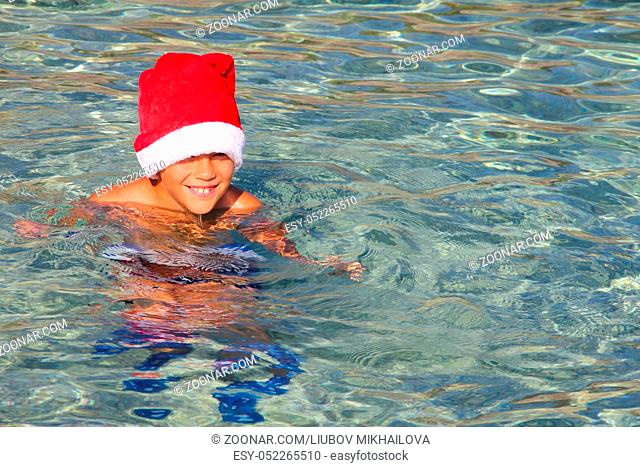 Boy in Santa Claus hat swimming in sea, Christmas vacation at sea concept