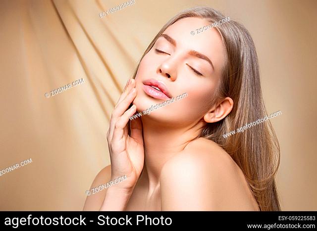 Beautiful young woman with perfect skin and shiny hair touching face over beige background. Beauty shot. Copy space