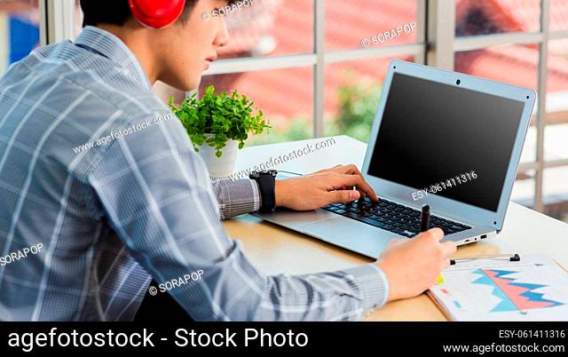 Asian businessman writing notes with pen inspired ideas list on paper notepad while working on laptop computer. Happy handsome man sitting busy on desk table...