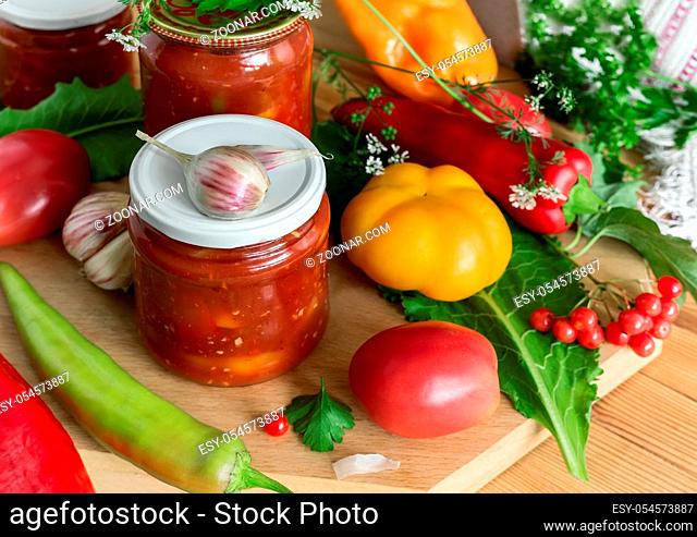 In glass jars Lecho of canned bell peppers and tomatoes, near fresh peppers and tomatoes