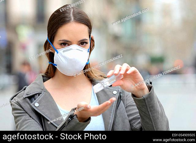 Portrait of a serious woman with protective mask using hand sanitizer looking at camera on street