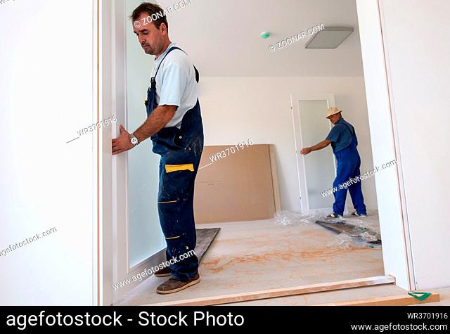 male workers carpenters installing interior glass door with a wooden frame at new luxury apartment